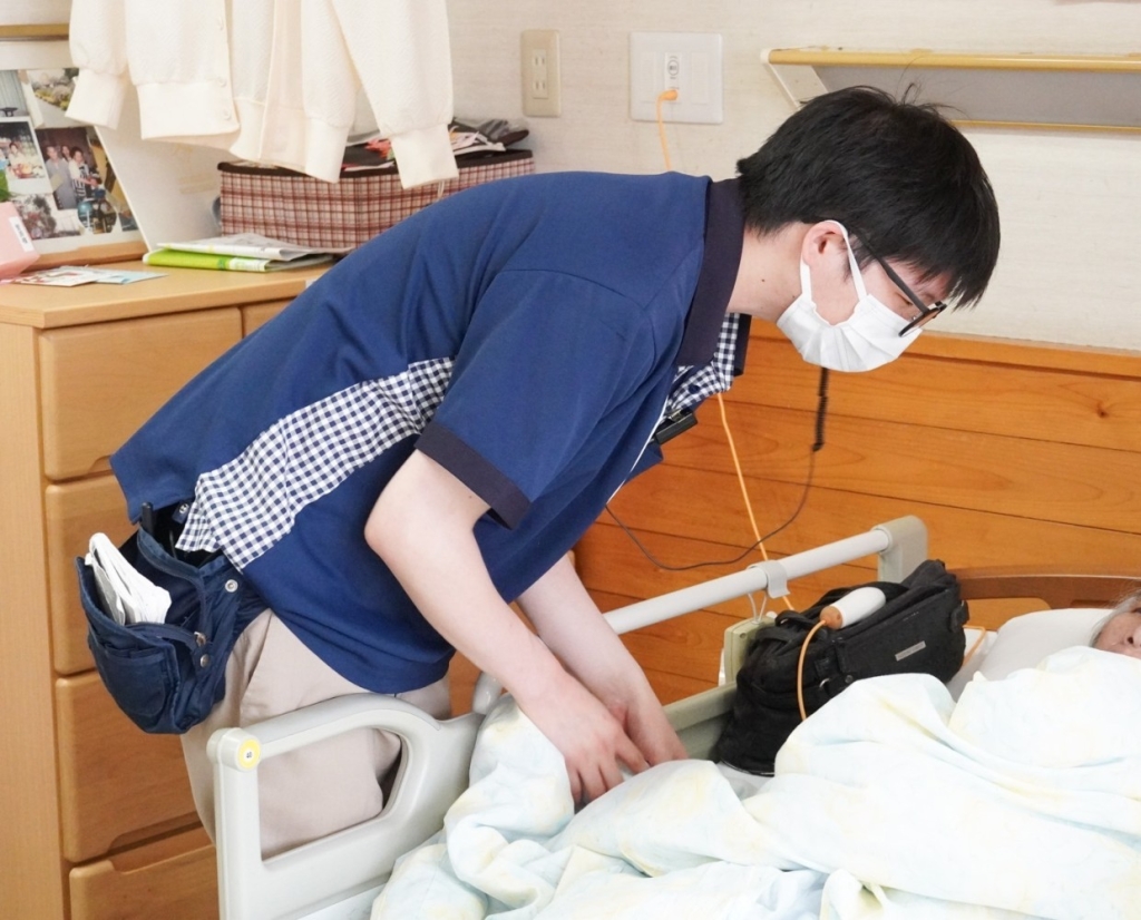 ベットに寝ている利用者さんとお話しする八木さん